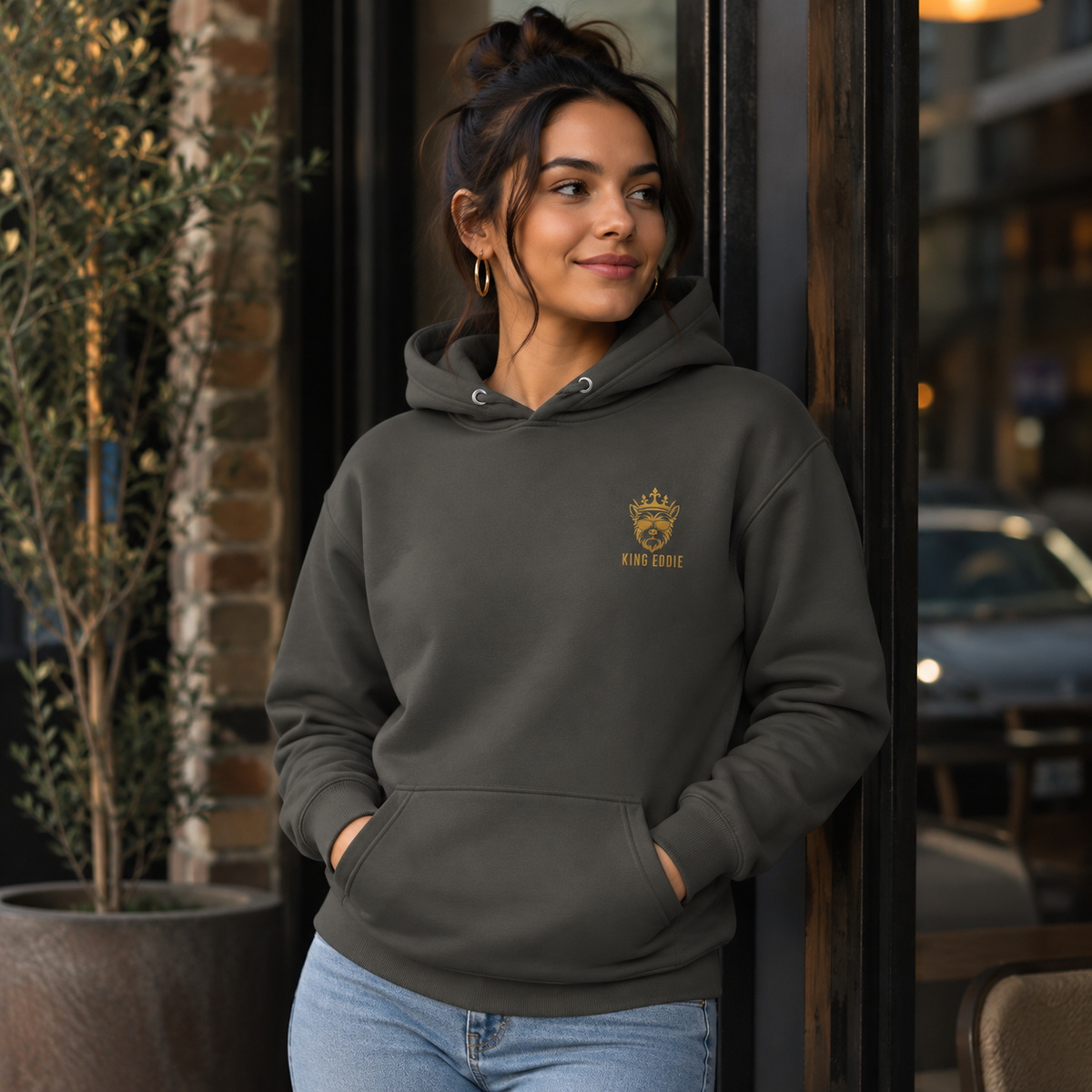 Woman wearing vintage black King Eddie Heritage Hoodie with gold crest logo outside a café