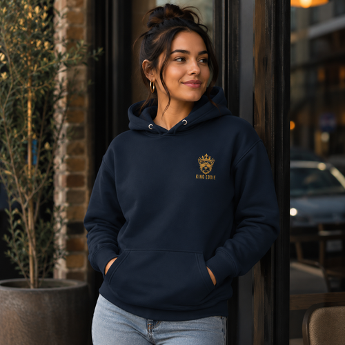 Woman wearing navy King Eddie Heritage Hoodie with gold crest logo outside a café